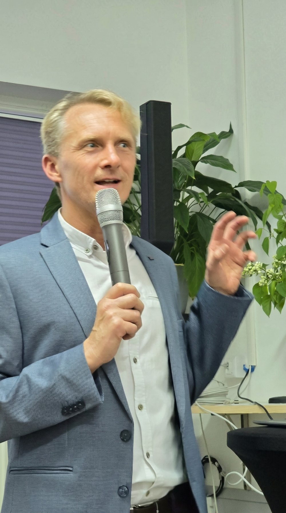 Dr Jerzy Lewko podczas wykładu, z mikrofonem, na tle zieleni i gałązek bzu